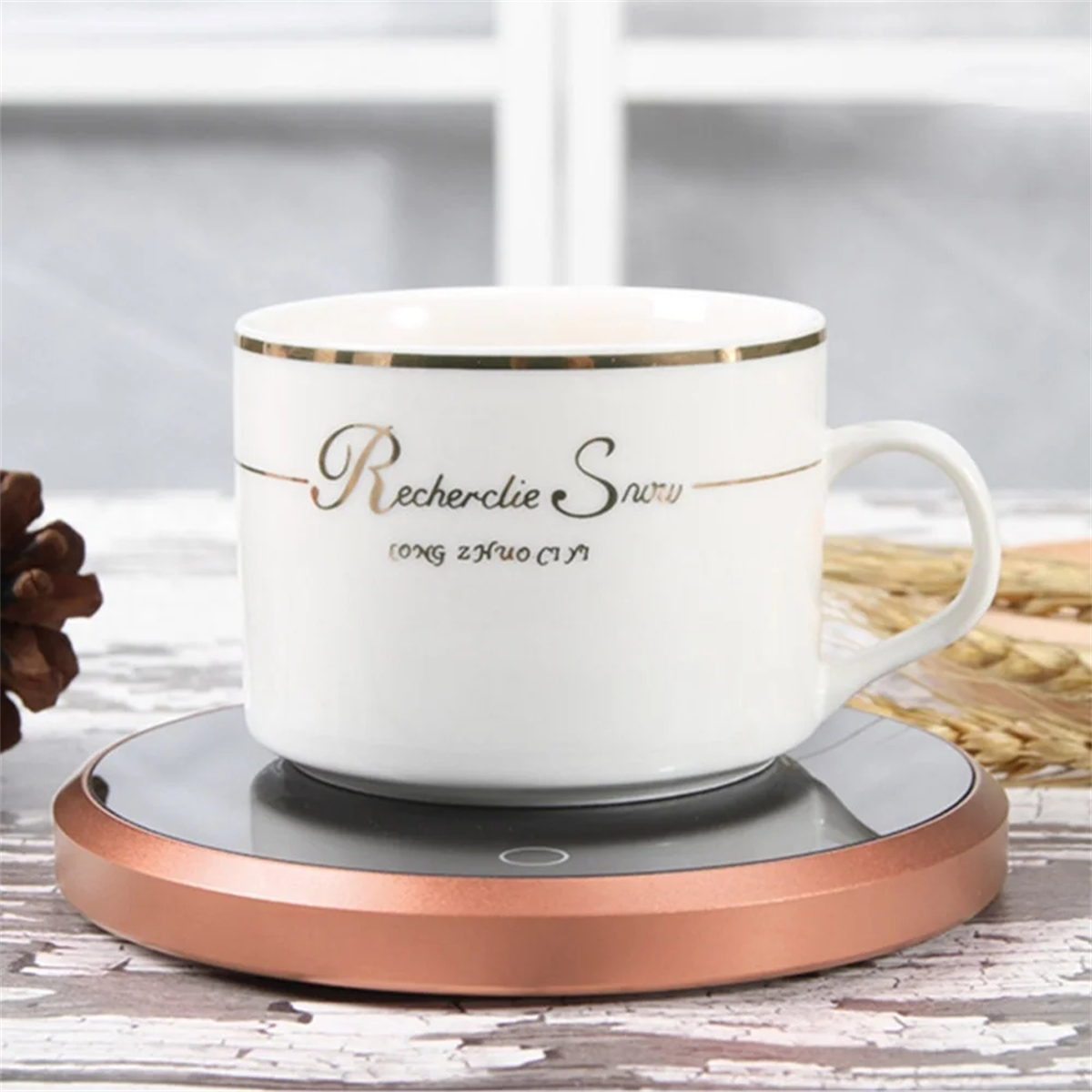 Weiße Tasse auf einem roségoldenen Wärmer. Die Tasse hat goldenen Text: Recherlie Snurv.