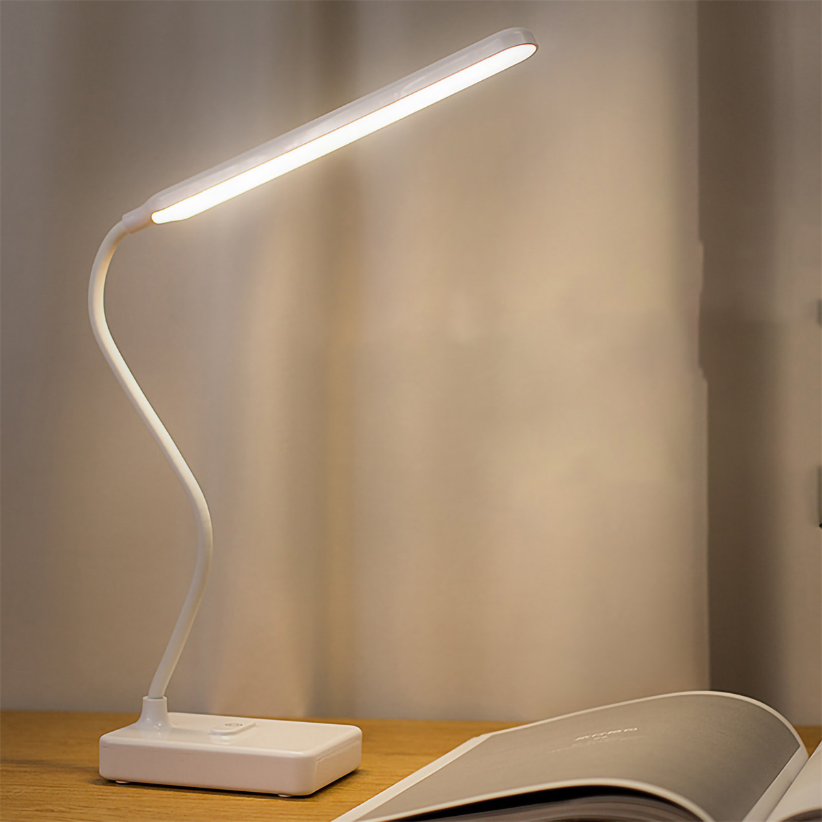 Weiße Schreibtischlampe mit gebogenem Arm, beleuchtet ein offenes Buch auf einem Schreibtisch.
