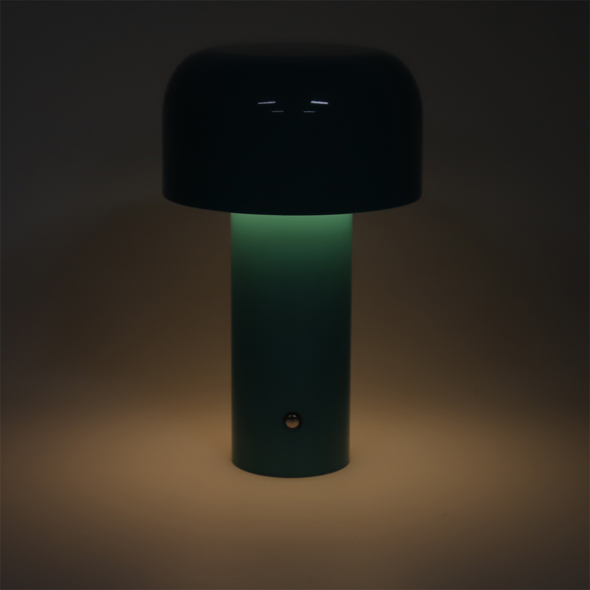 Eine teal-farbene Lampe mit rundem Oberteil und zylindrischem Sockel, die einen grünen Schein wirft.