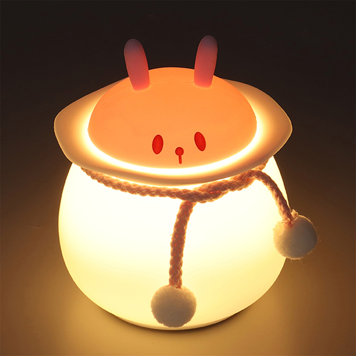 Hasenförmiges Nachtlicht, leuchtend. Rosa Ohren, rote Nase und weiße Bommel. Dunkler Hintergrund.