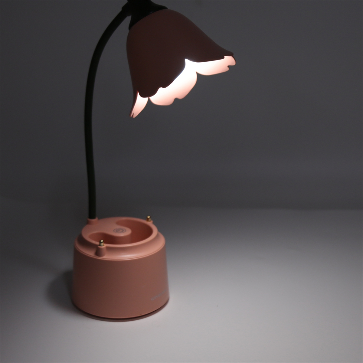 Eine rosa Lampe mit einem blütenförmigen Schirm. Sie steht auf einem Tisch und hat einen dunklen Hintergrund.