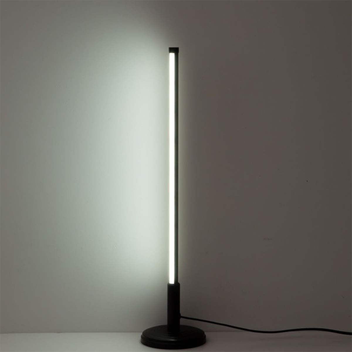 Eine hohe, schwarze Stehlampe mit hellem, vertikalem Licht und weißem Wandhintergrund.