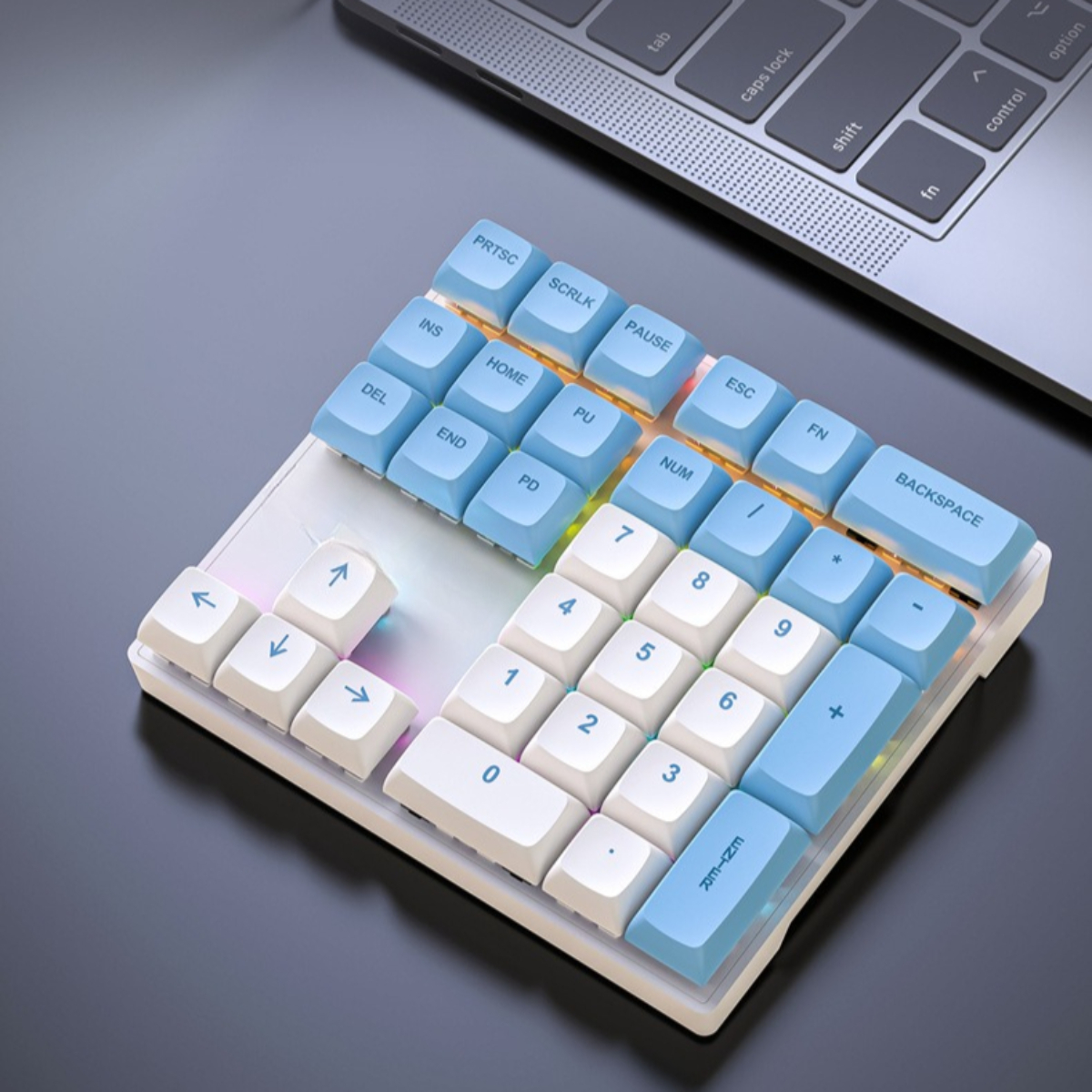 Mechanische Tastatur mit blau-weißen Tasten, auf dunkler Oberfläche, neben Laptop.