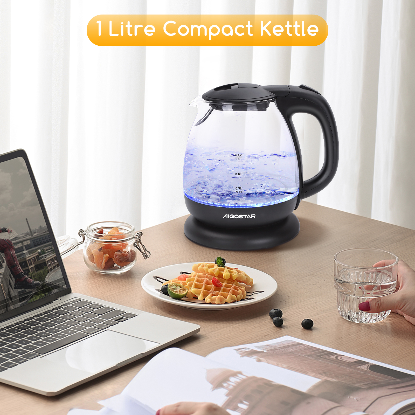 Hervidor eléctrico de vidrio transparente con luz azul. Está sobre una mesa con gofres, fruta y una laptop.