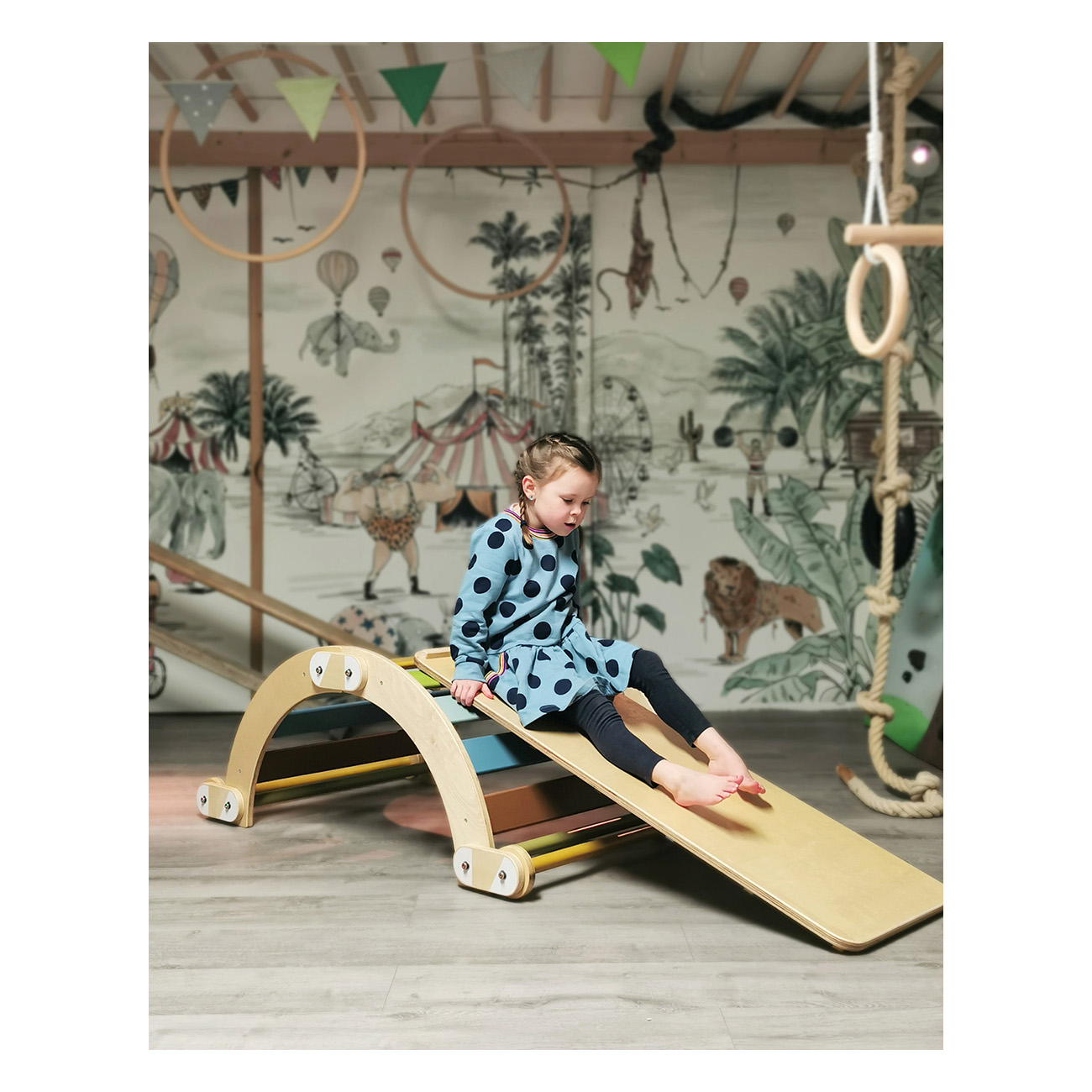 Ein Mädchen auf einer Holz-Kletterstruktur in einem Zimmer mit Zirkus-Kunst.