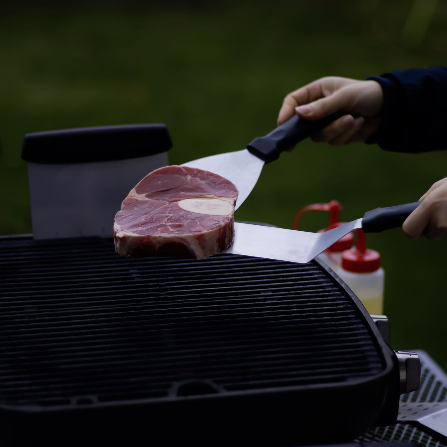 Hände, die Spatel benutzen, um ein Steak auf einem Grill zu wenden.