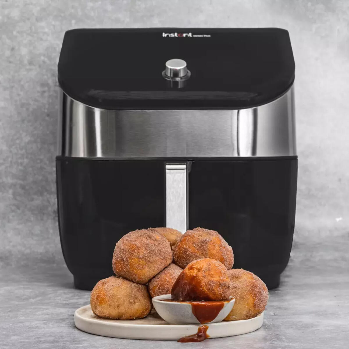 Schwarze Heißluftfritteuse mit Donuts und Dip-Soße auf einem Teller.