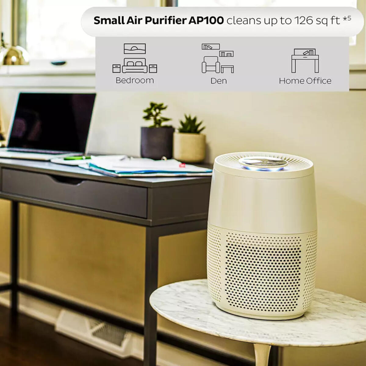 Petit purificateur d'air sur une table. Il a un corps blanc et un dessus gris foncé, avec une petite plante à côté.