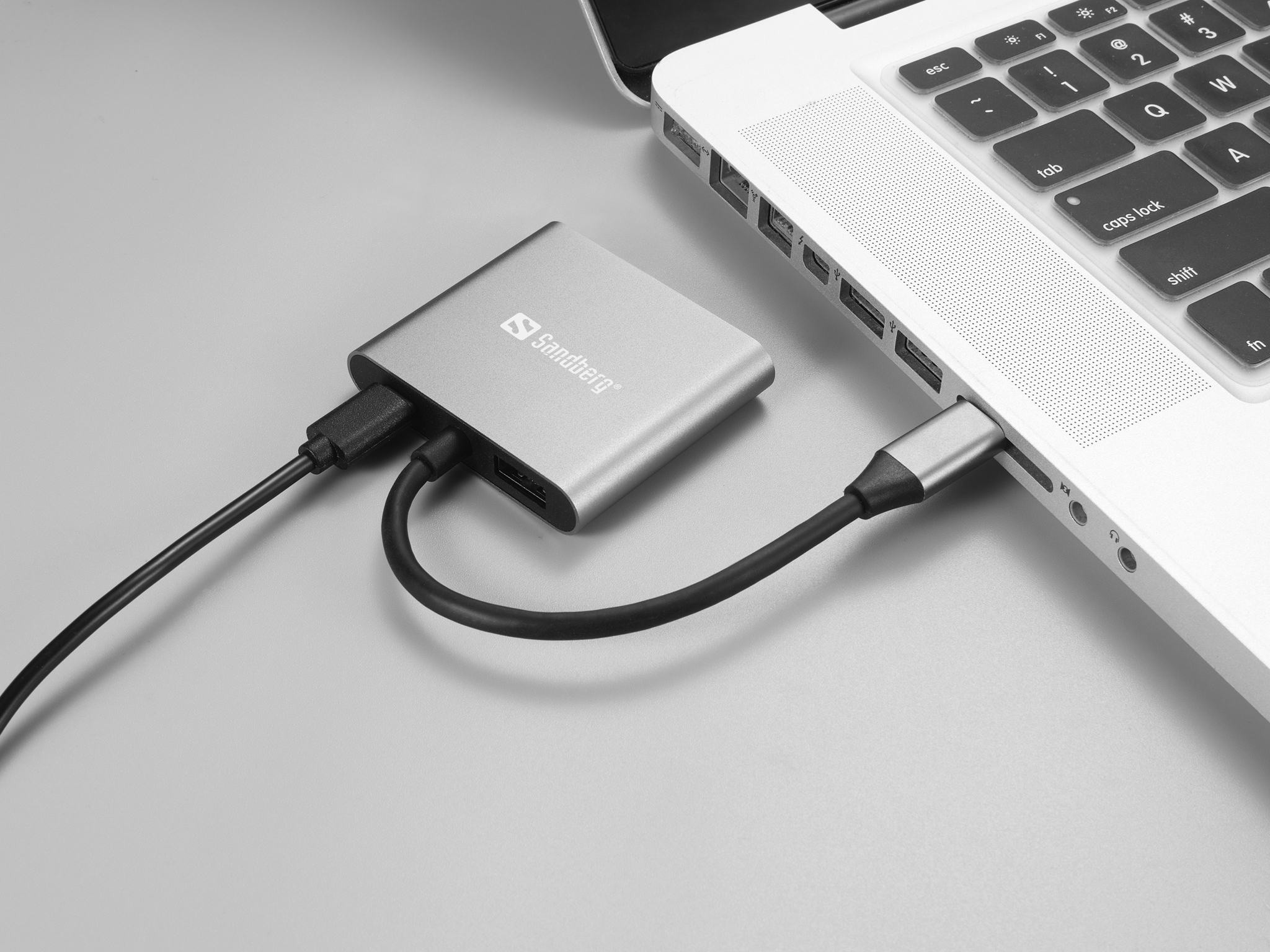 Silberner USB-Hub mit einem schwarzen Kabel an einem Laptop angeschlossen.