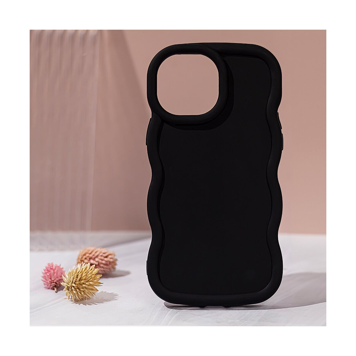 Una custodia nera per telefono con bordi ondulati e tre piccoli fiori su una superficie bianca.