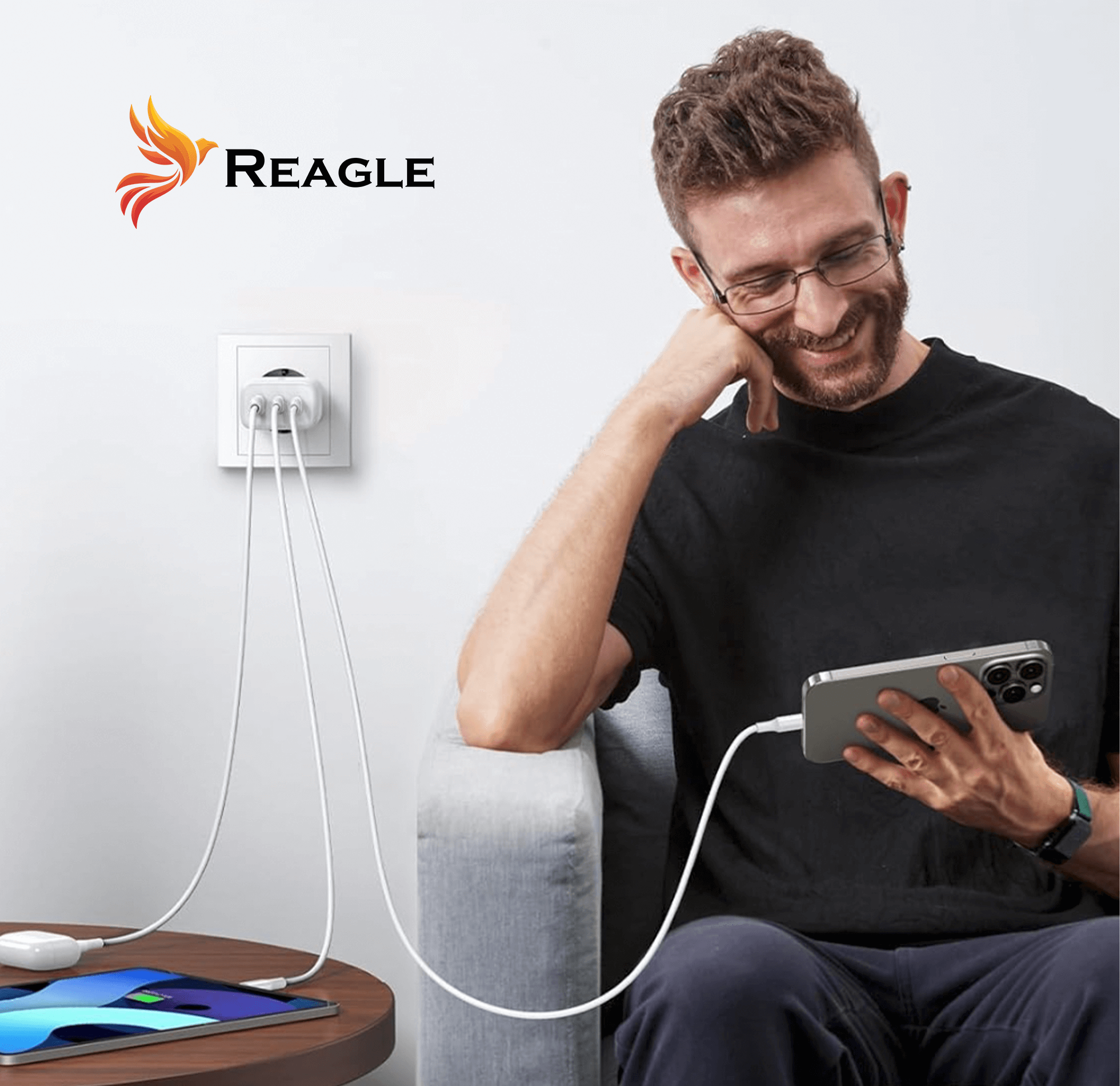 Mężczyzna korzystający z telefonu ładującego się oraz tablet ładujący się na stole, biała ściana.