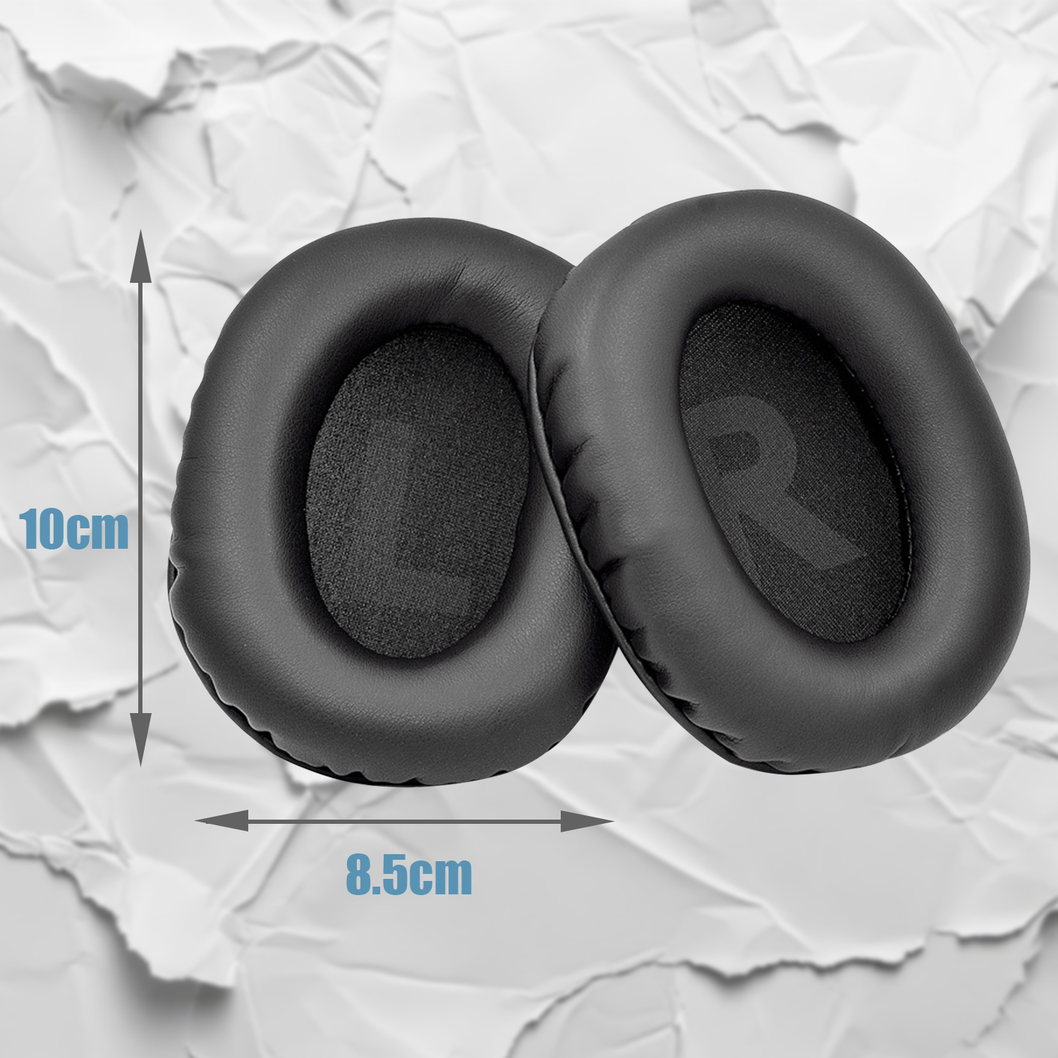 Dwie czarne poduszki na uszy leżące na pomiętym papierze, z wymiarami.
