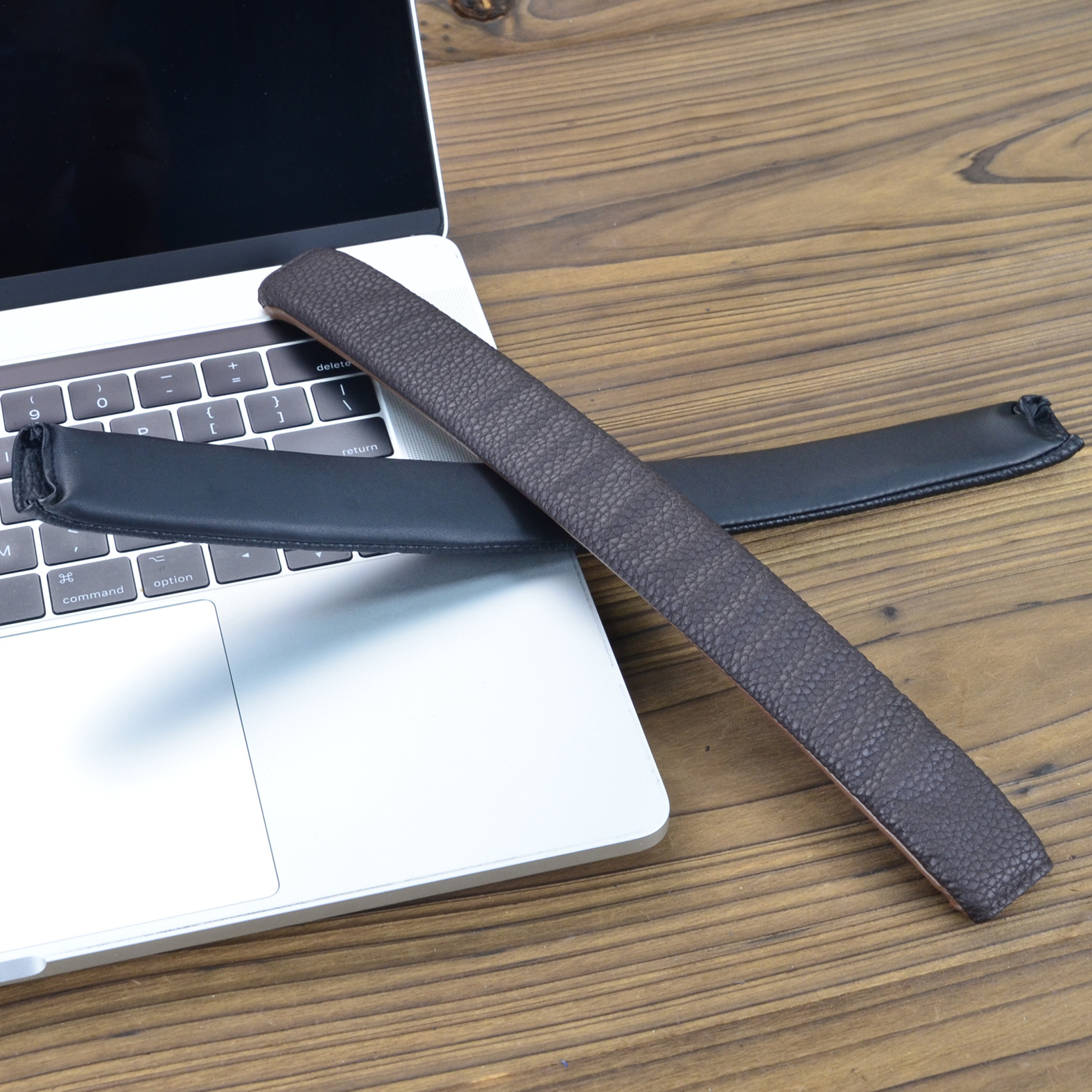 Twee donkerbruine en zwarte leren polssteunkussens voor laptops, geplaatst op een laptoptoetsenbord.