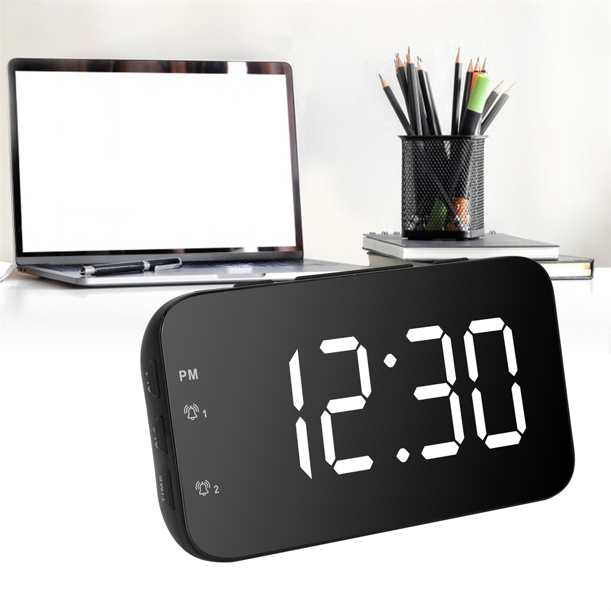 Schwarzer digitaler Wecker mit 12:30. Laptop und Stifthalter mit Stiften im Hintergrund.