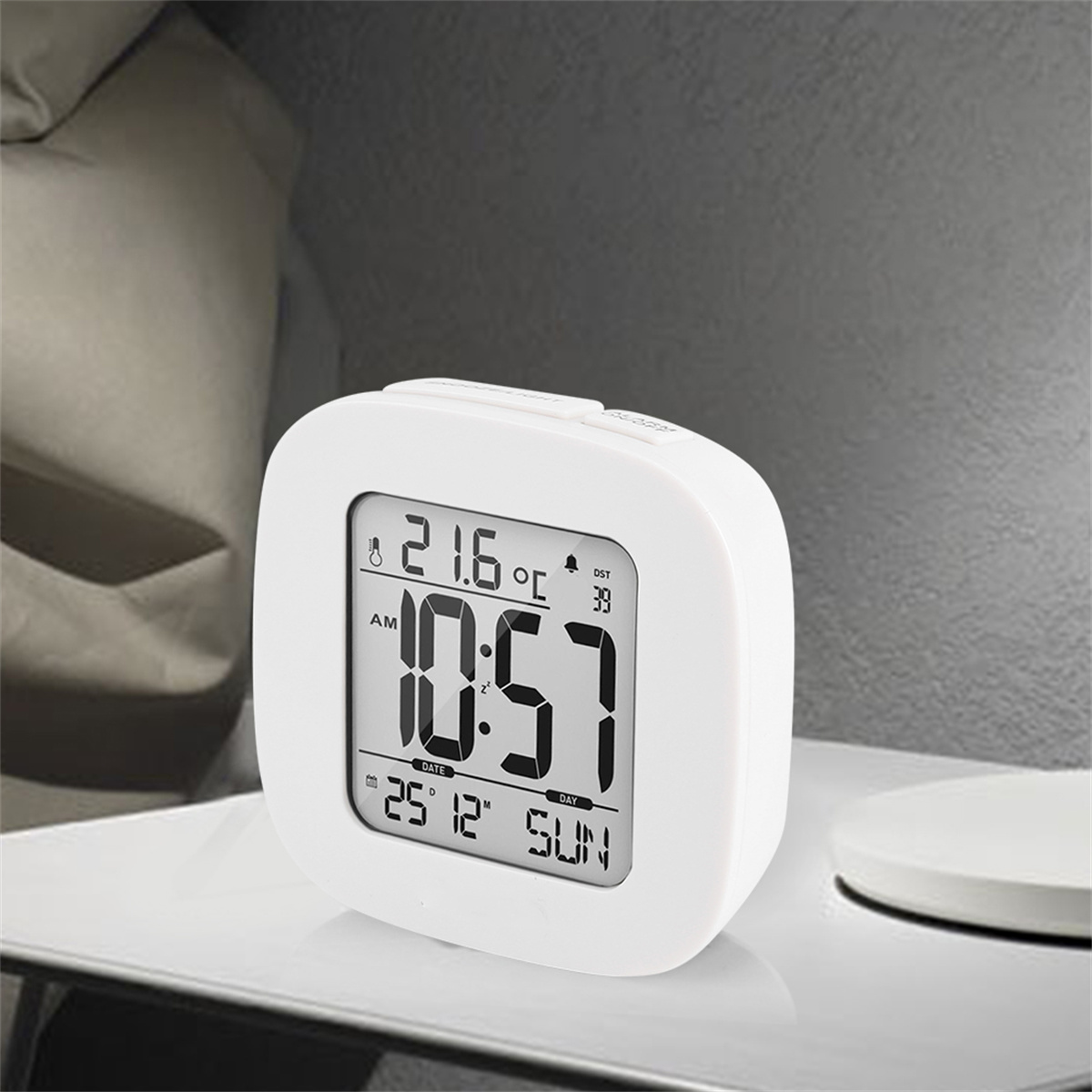 Eine weiße Digitaluhr zeigt Uhrzeit, Datum und Temperatur an. Sie steht auf einer weißen Oberfläche.