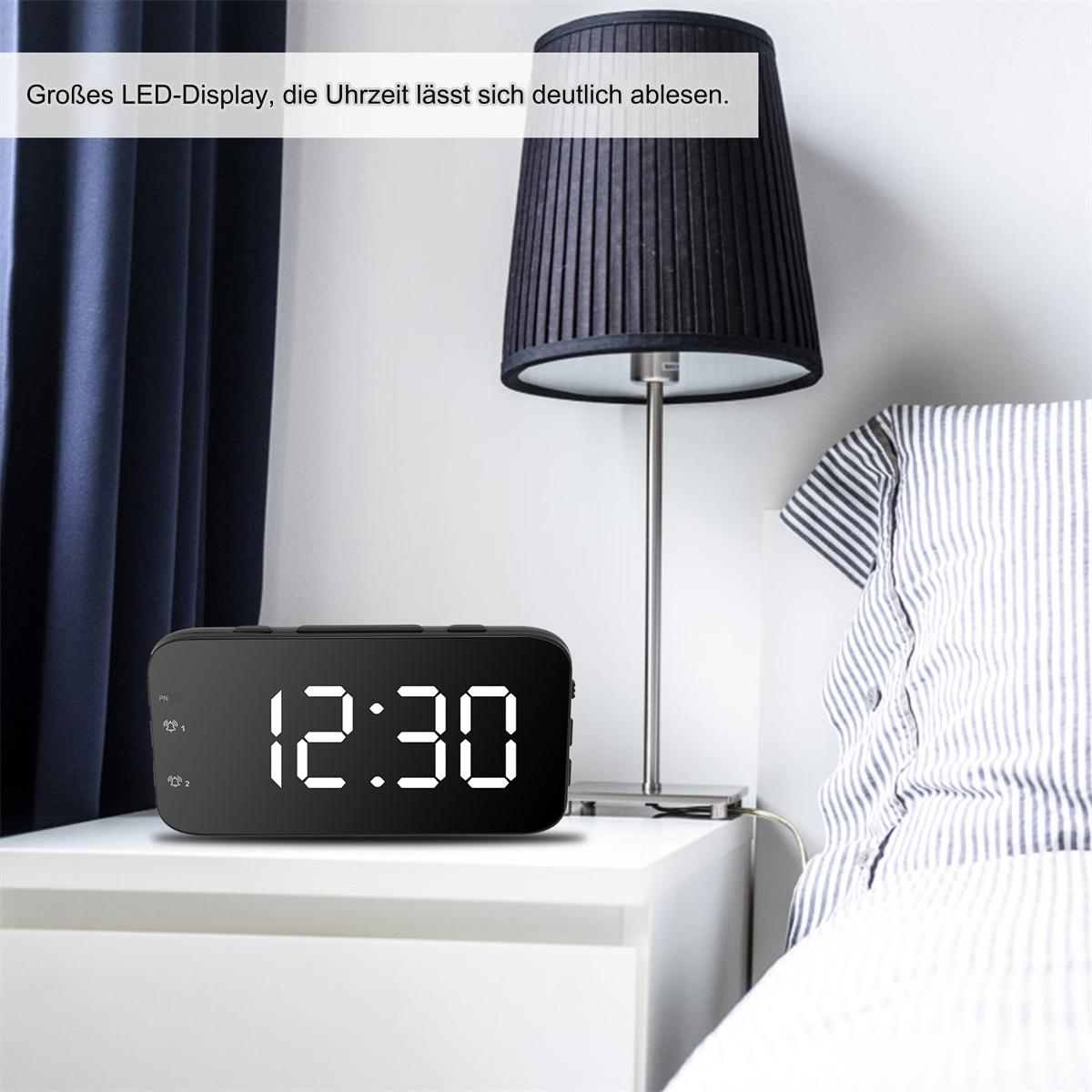 Schwarze Digitaluhr, die 12:30 Uhr anzeigt, auf einem weißen Nachttisch neben einer Lampe.