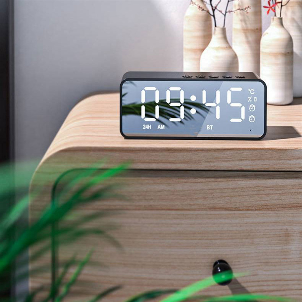 Ein schwarzer digitaler Wecker auf einem Nachttisch aus Holz. Zeigt 09:45.