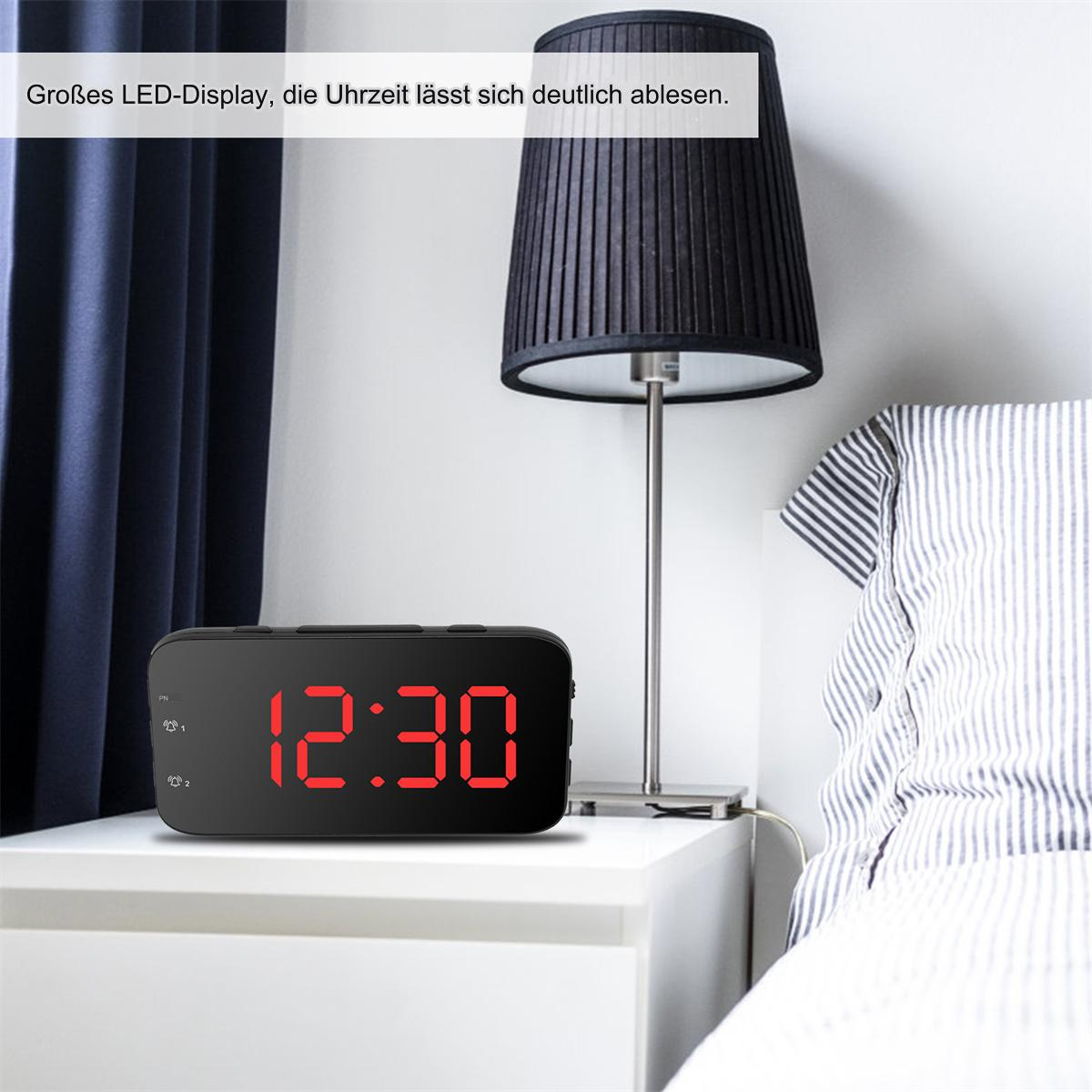 Schwarze Digitaluhr auf einem weißen Nachttisch. Die angezeigte Uhrzeit ist 12:30 Uhr. Über der Uhr ist eine Lampe.