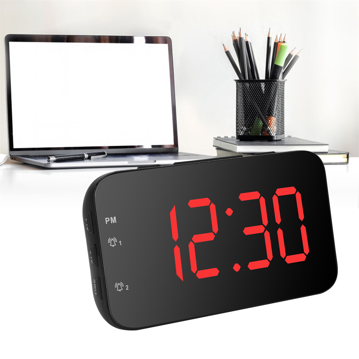 Eine schwarze Digitaluhr mit roten Zahlen zeigt 12:30 an. Ein Laptop und Stifte in einem Halter sind im Hintergrund.