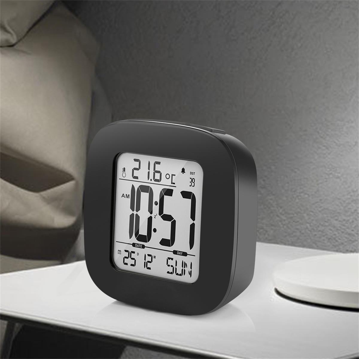 Schwarzer digitaler Wecker mit Zeit, Datum und Temperatur auf weißer Oberfläche.