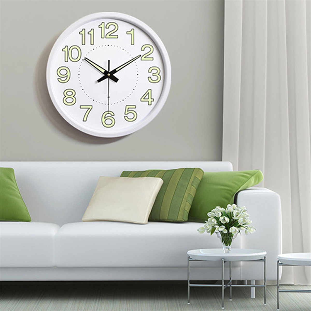 Eine weiße Wanduhr an einer grauen Wand, mit weißem Sofa und grünen Kissen.