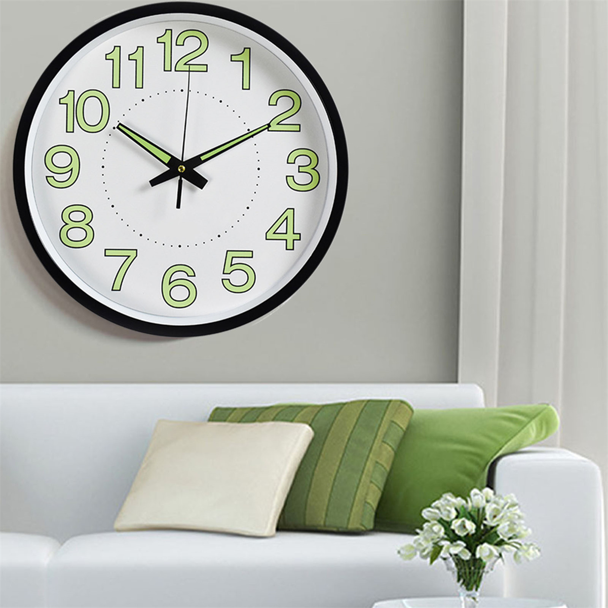 Wanduhr mit grün leuchtenden Zahlen und Zeigern sowie einem weißen Sofa mit Kissen.
