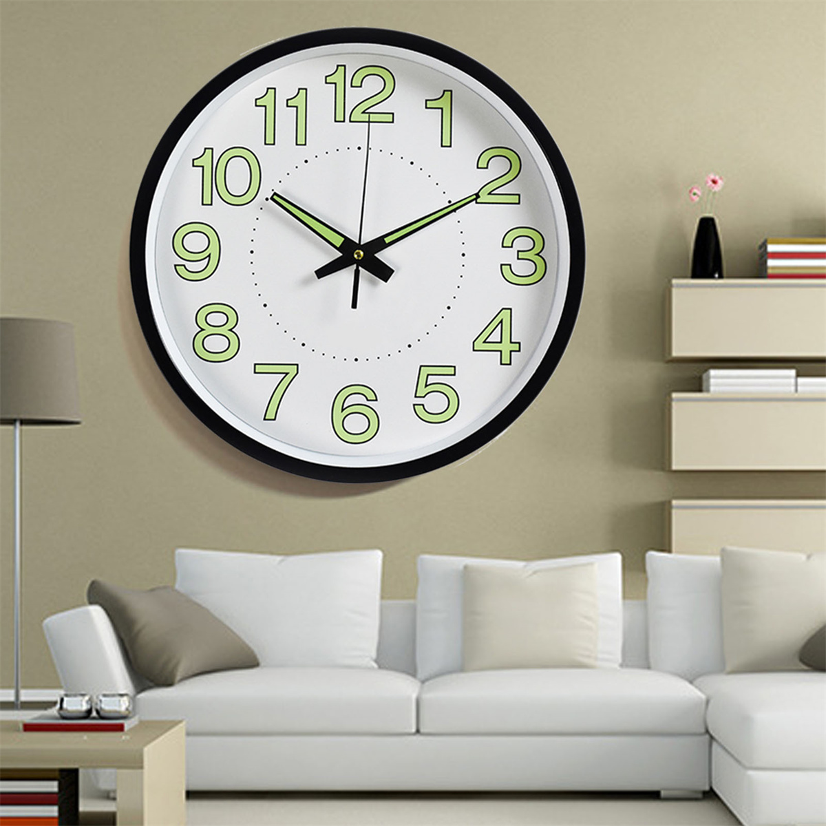 Wanduhr mit schwarzem Rahmen, weißem Zifferblatt und grünen Ziffern, Zeiger zeigen 9:50. Sofa im Hintergrund.