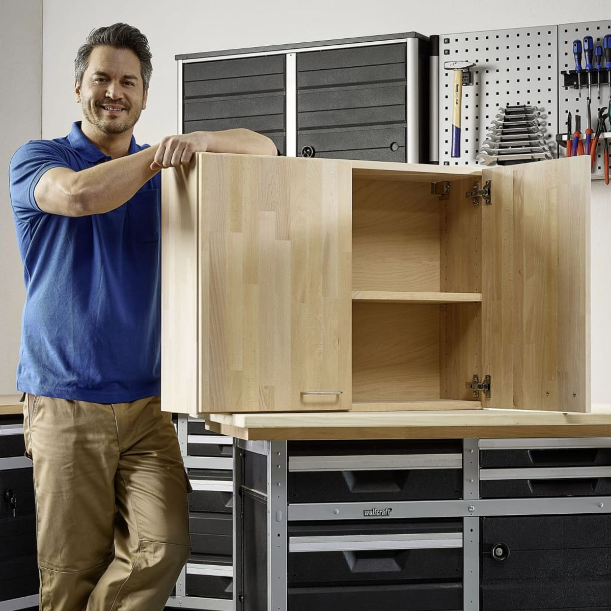 Ein Mann in blauem Hemd steht neben einem offenen Holzschrank über einer Schubladenreihe.