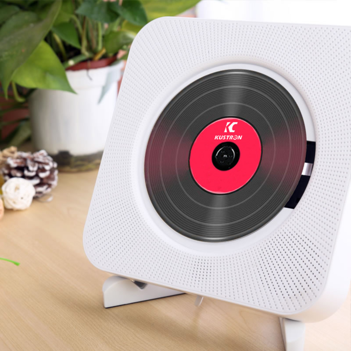 Weißer CD-Player mit roter Disc. Grüne Pflanze im Hintergrund.