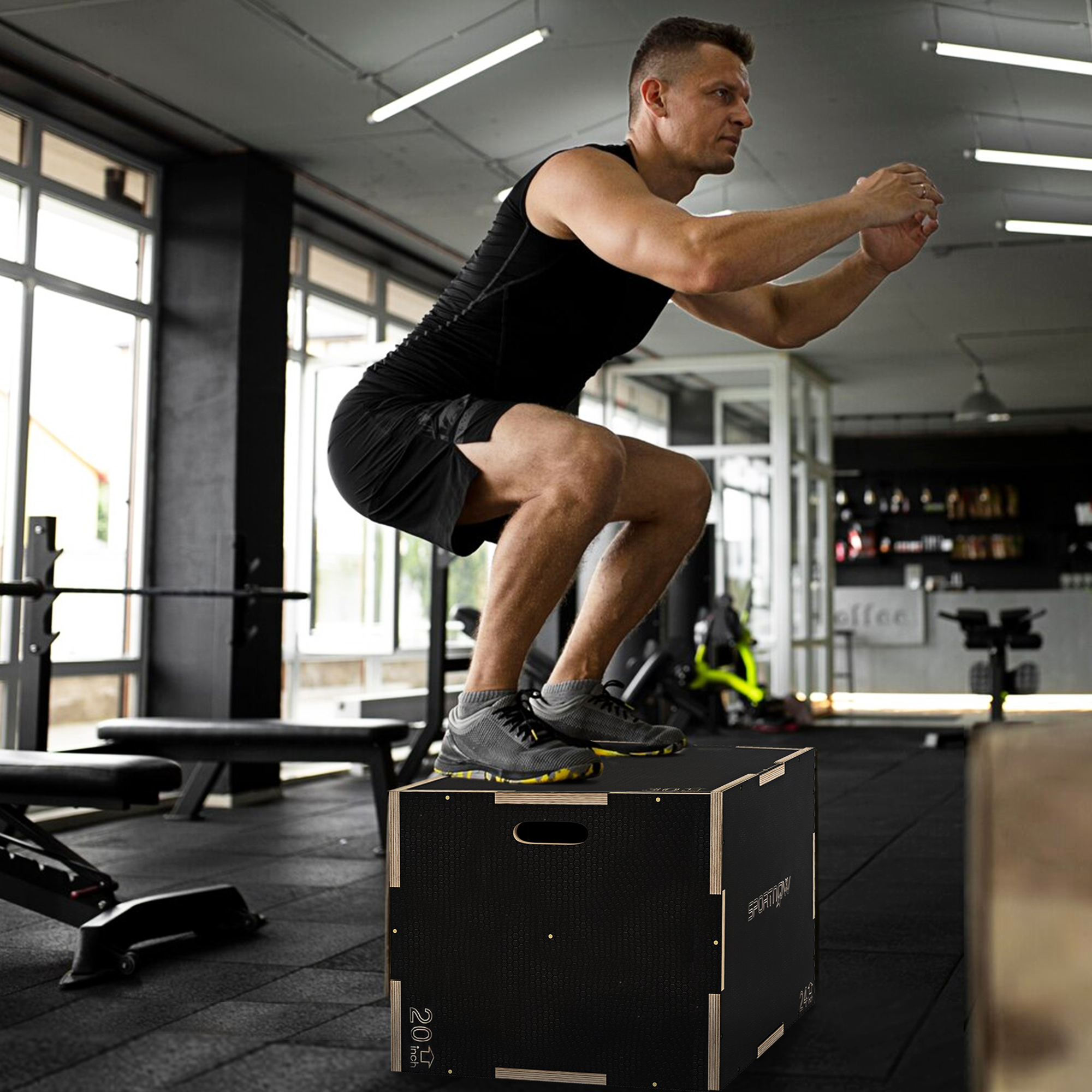 Hombre en ropa deportiva negra haciendo ejercicio de salto de caja en un gimnasio con caja negra.