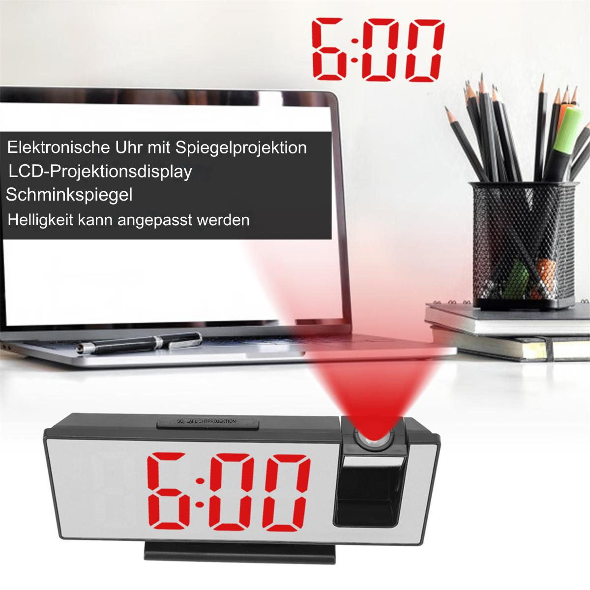 Eine Digitaluhr projiziert die Uhrzeit 6:00 an die Wand. Laptop und Stifte im Hintergrund.