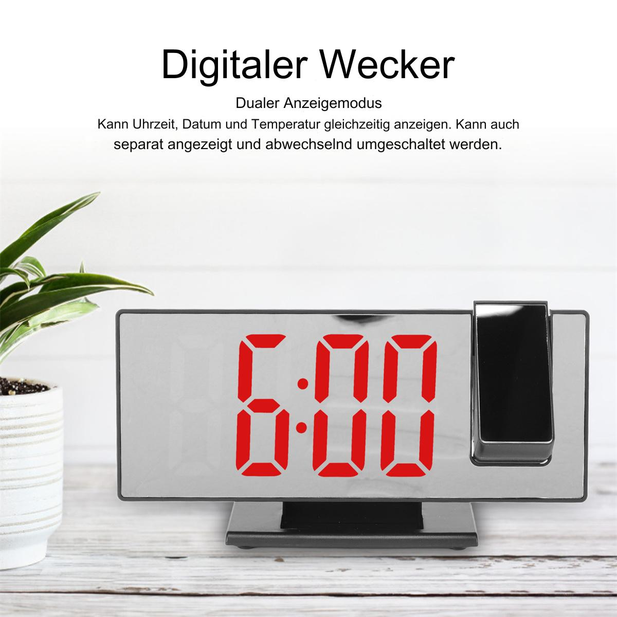 Digitaluhr mit roten Ziffern, die 6:00 anzeigen. Projektor rechts. Weißer Tisch, Pflanze.