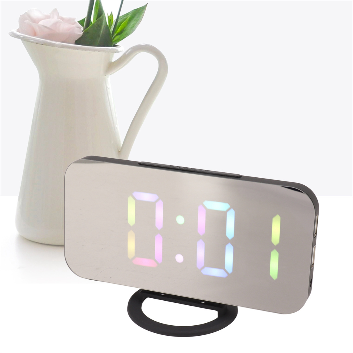 Eine silberne Digitaluhr zeigt 0:01 mit einer rosa Blume in einer weißen Vase an.