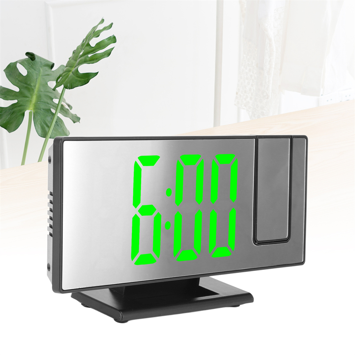 Digitaler Wecker mit grünen Zahlen, die 6:00 anzeigen, auf einem Tisch.