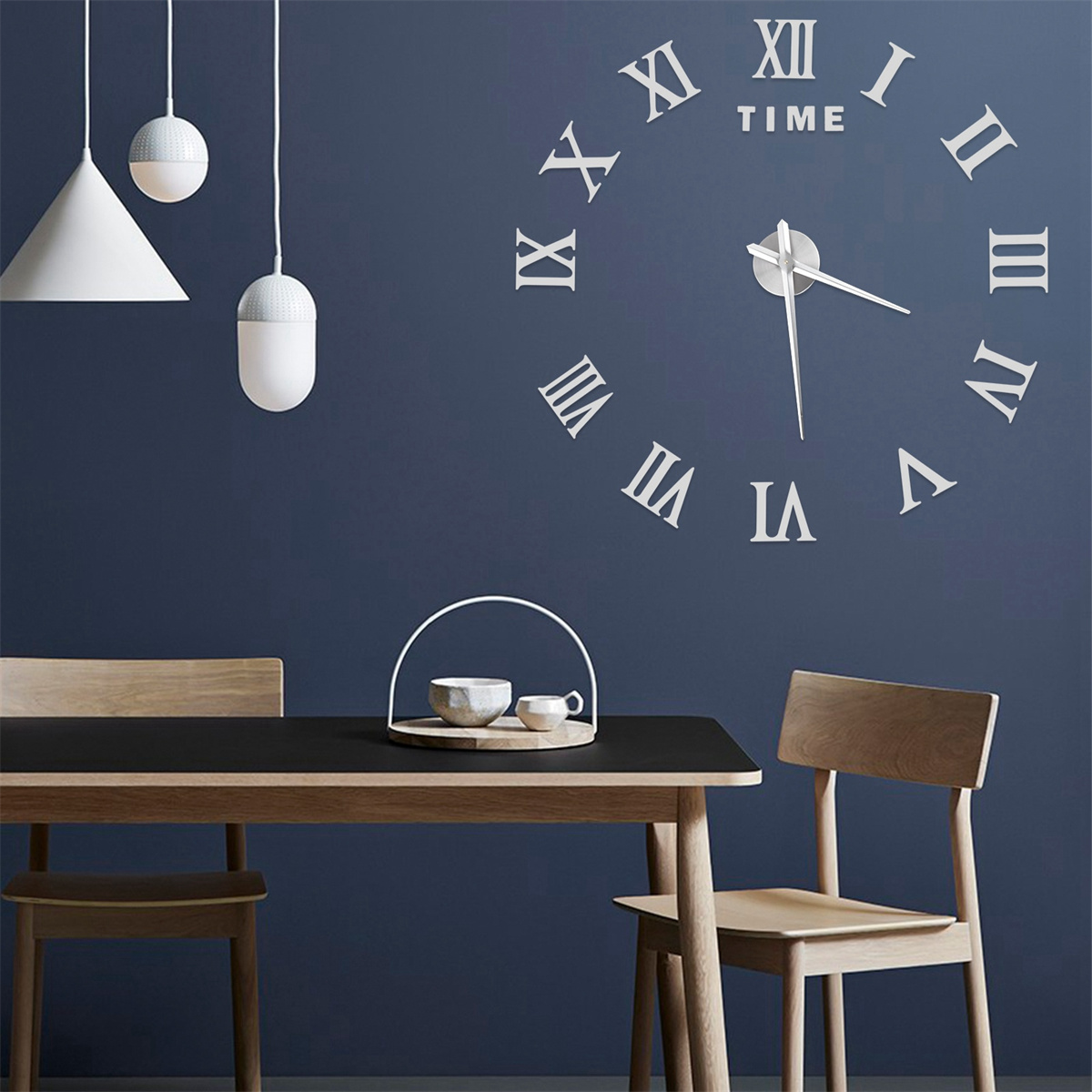 Große Wanduhr mit römischen Ziffern und Uhrzeigern. Zwei Hängelampen und ein Tisch im Raum.