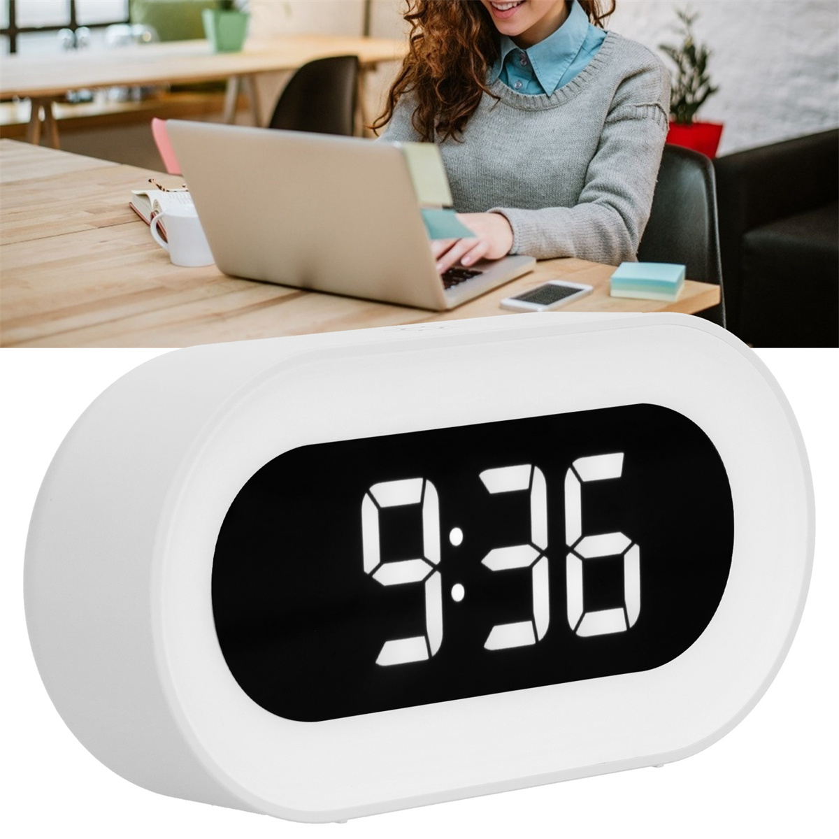 Eine weiße Digitaluhr mit der Anzeige 9:36, im Hintergrund arbeitet eine Person an einem Laptop.