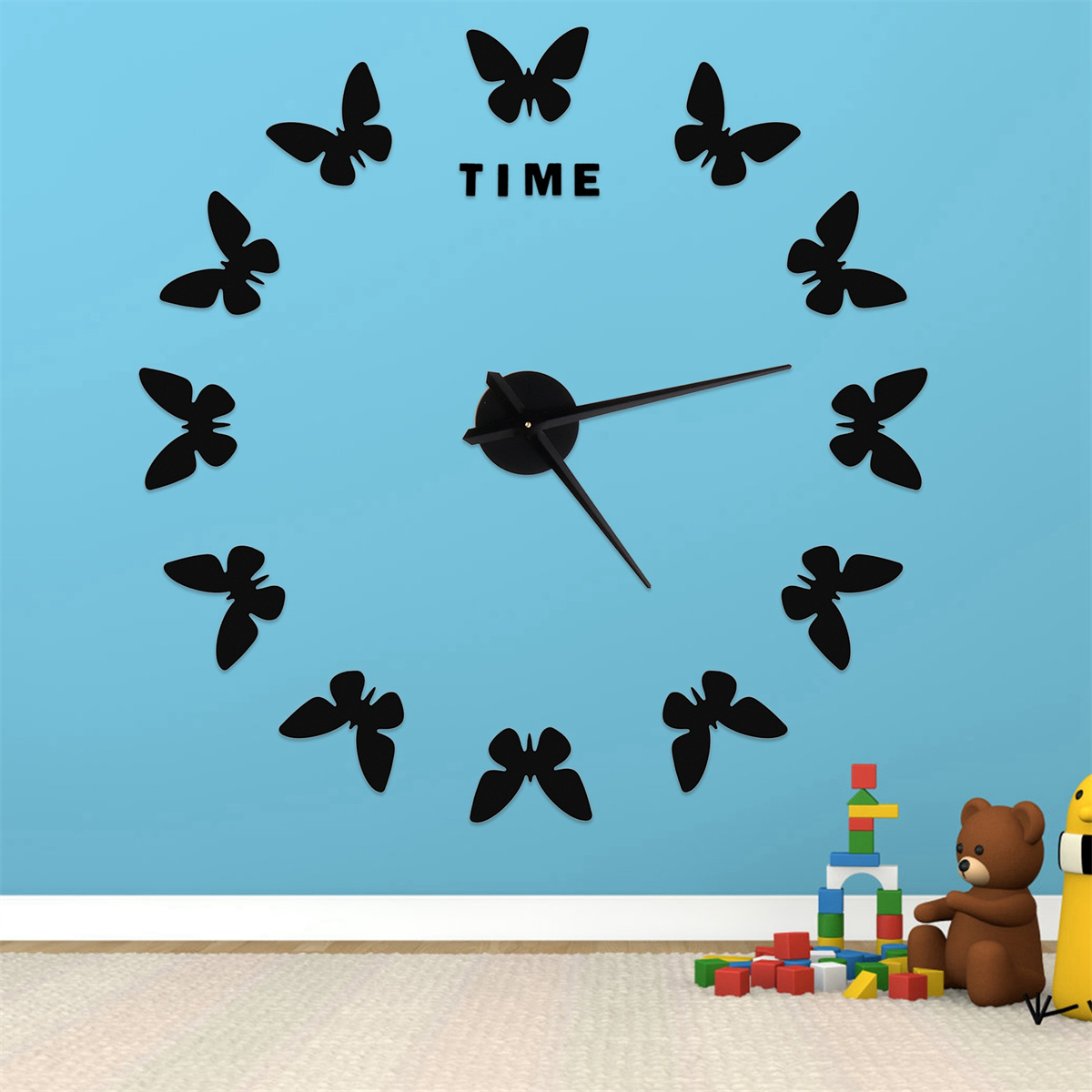 Wanduhr mit schwarzen Schmetterlingsformen für Zahlen. Sie hat schwarze Zeiger und einen blauen Wandhintergrund mit einem Spielzeug auf dem Boden.