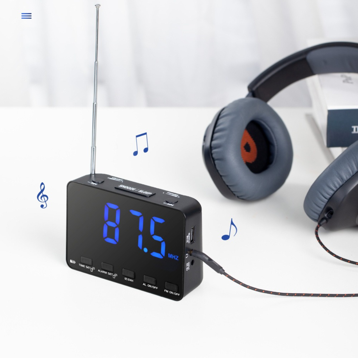 Schwarzes Digital-Radiowecker mit Kopfhörern und Noten auf weißer Oberfläche.