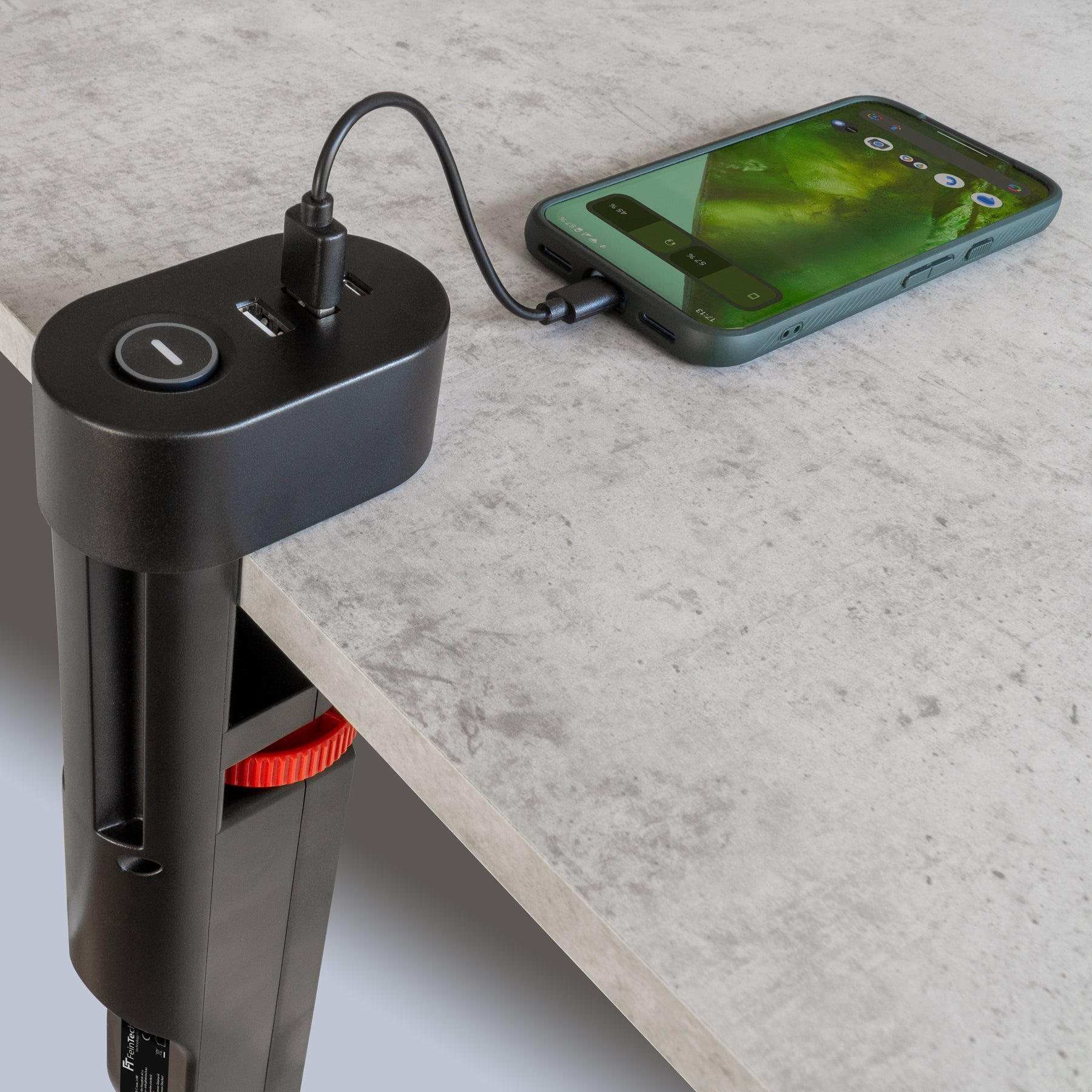 Schwarze Ladestation an einem Tisch befestigt. Ein Telefon ist angeschlossen.