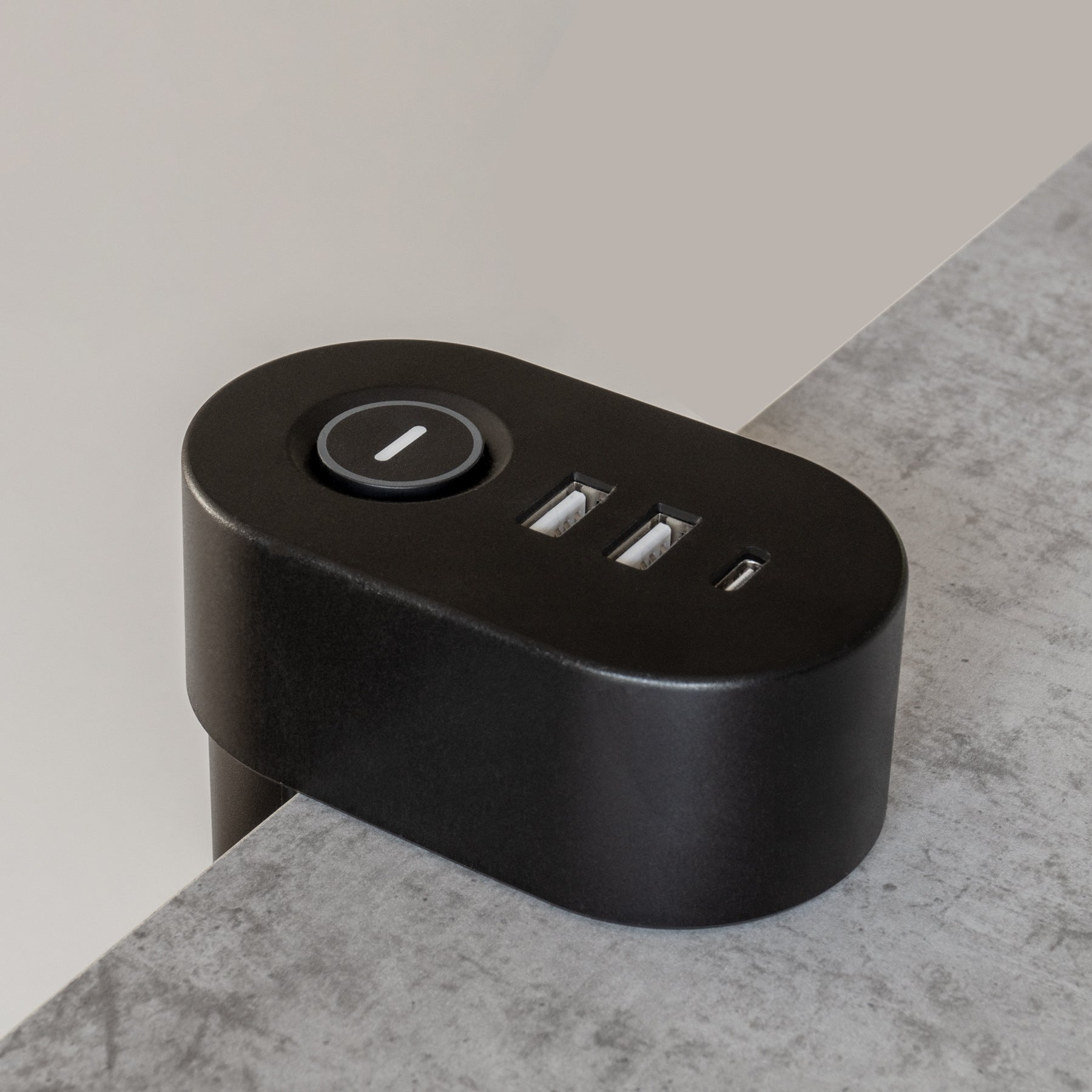 Schwarze Ladestation mit USB-Anschlüssen und Knopf. Grauer Hintergrund und Tisch.