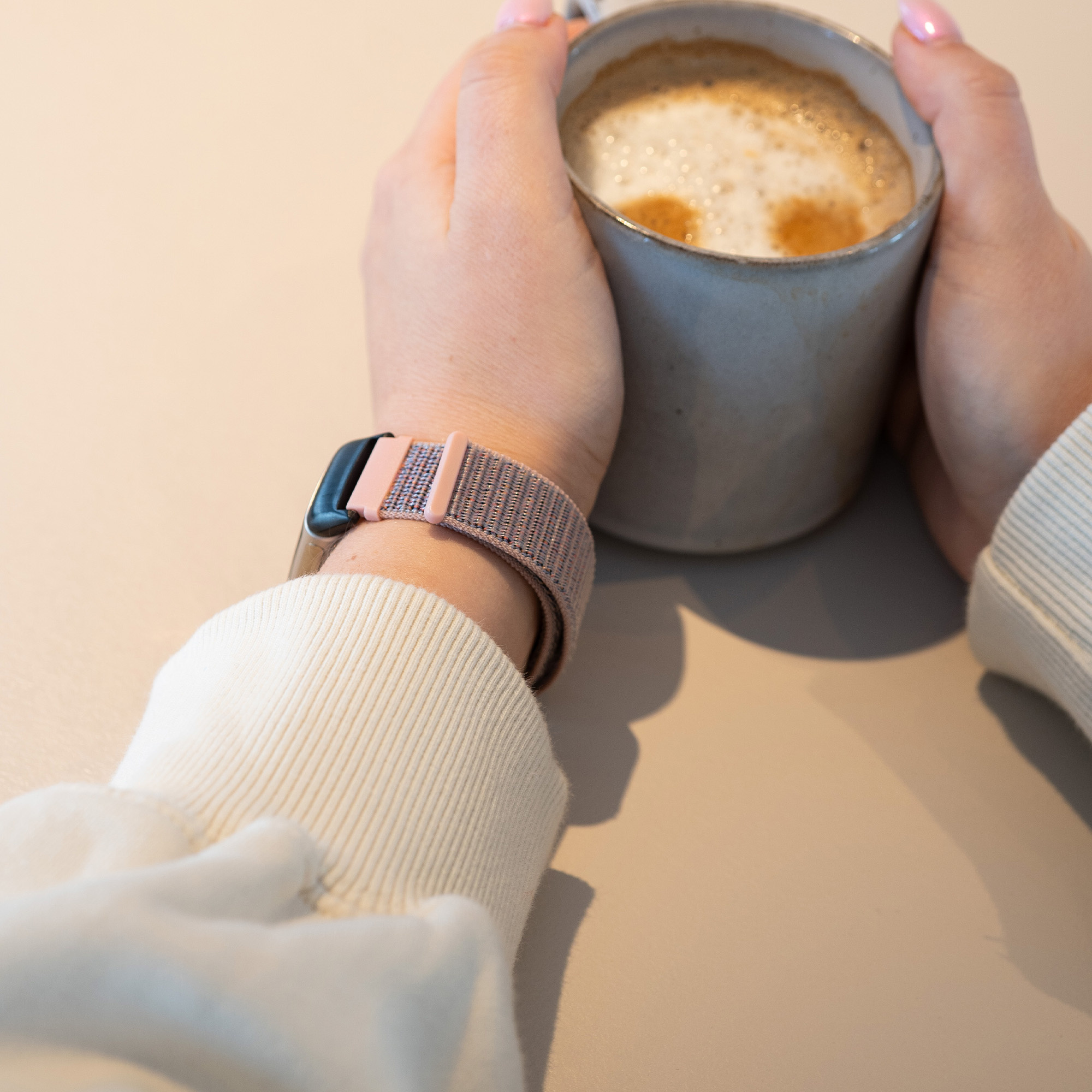 Person hält eine Tasse Kaffee, trägt eine Uhr mit rosa-grauem Band.