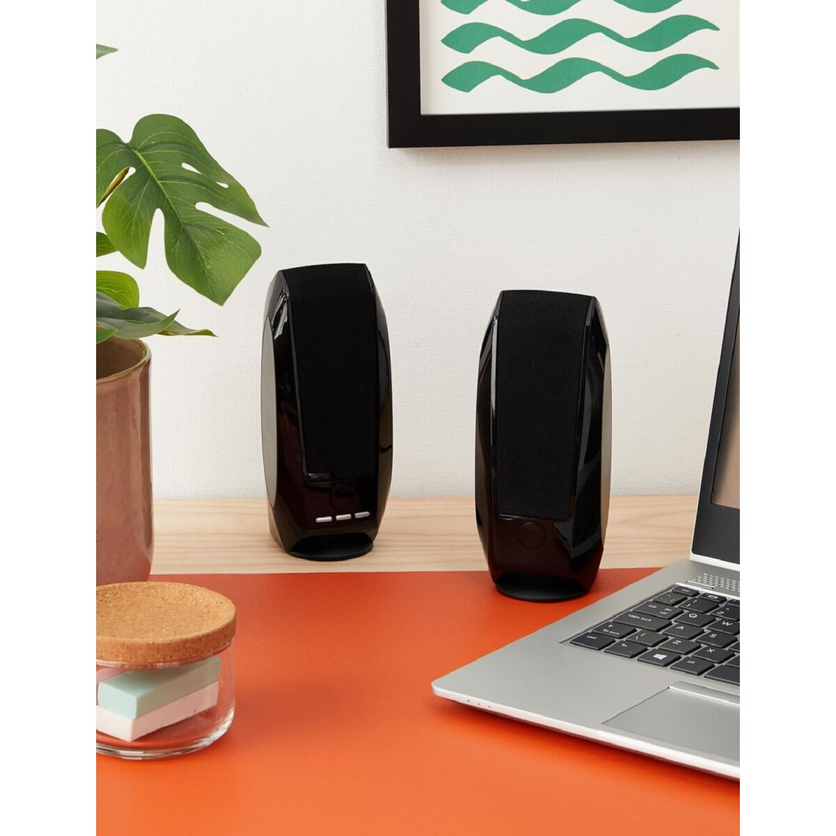 Dos altavoces negros sobre una superficie naranja, con portátil y decoración.