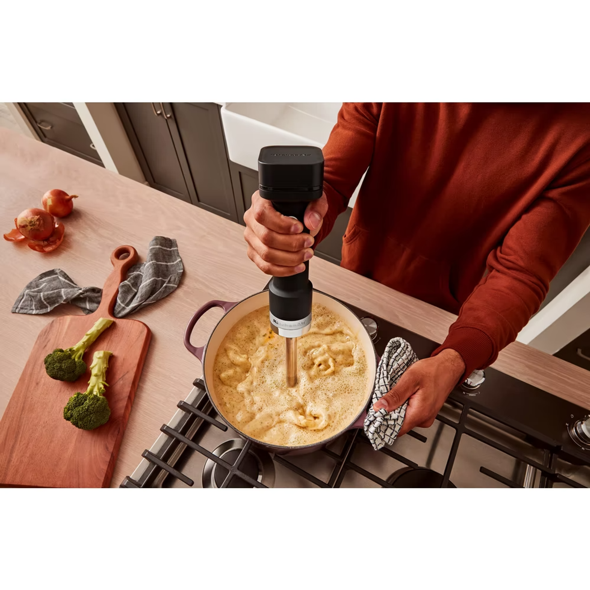 Personne utilisant un mixeur plongeant noir dans une casserole. Les ingrédients sont en cours de mélange.