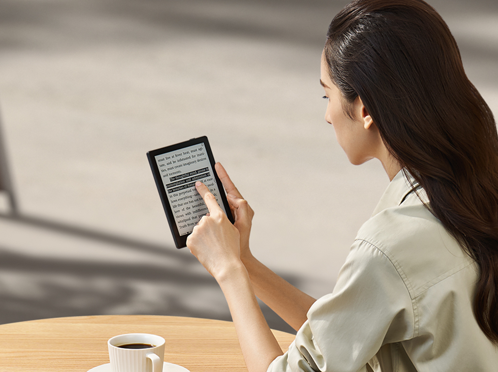 Kobieta czytająca czytnik e-booków z filiżanką kawy na stole. Światło słoneczne i rozmyte tło.