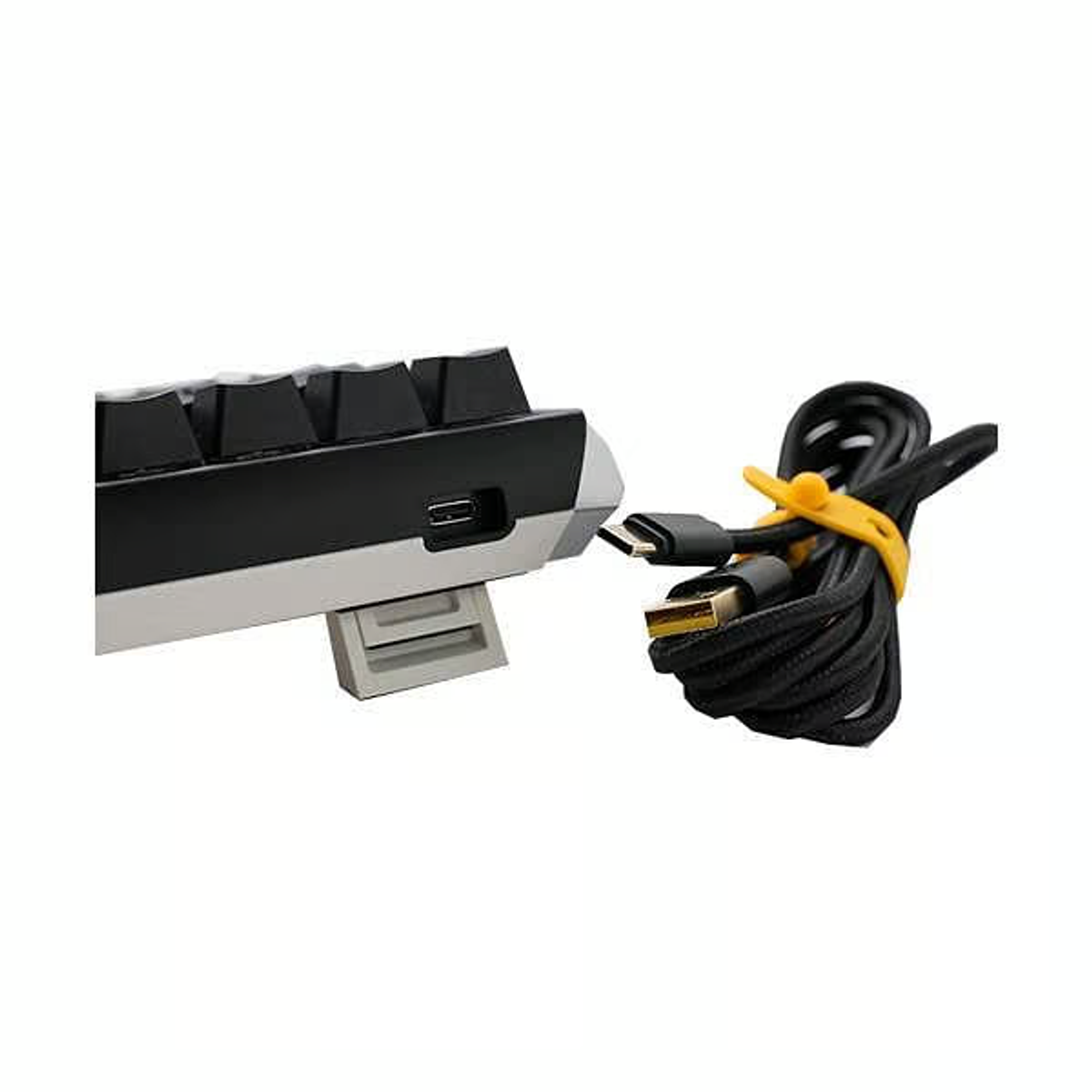 Una tastiera e un cavo USB-C con una fascetta gialla su una superficie bianca. La tastiera è in bianco e nero.