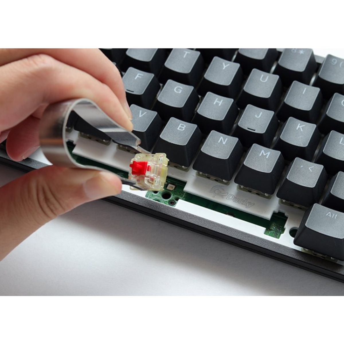 Una mano colocando un interruptor rojo en un teclado, mostrando las teclas y los componentes internos del teclado.