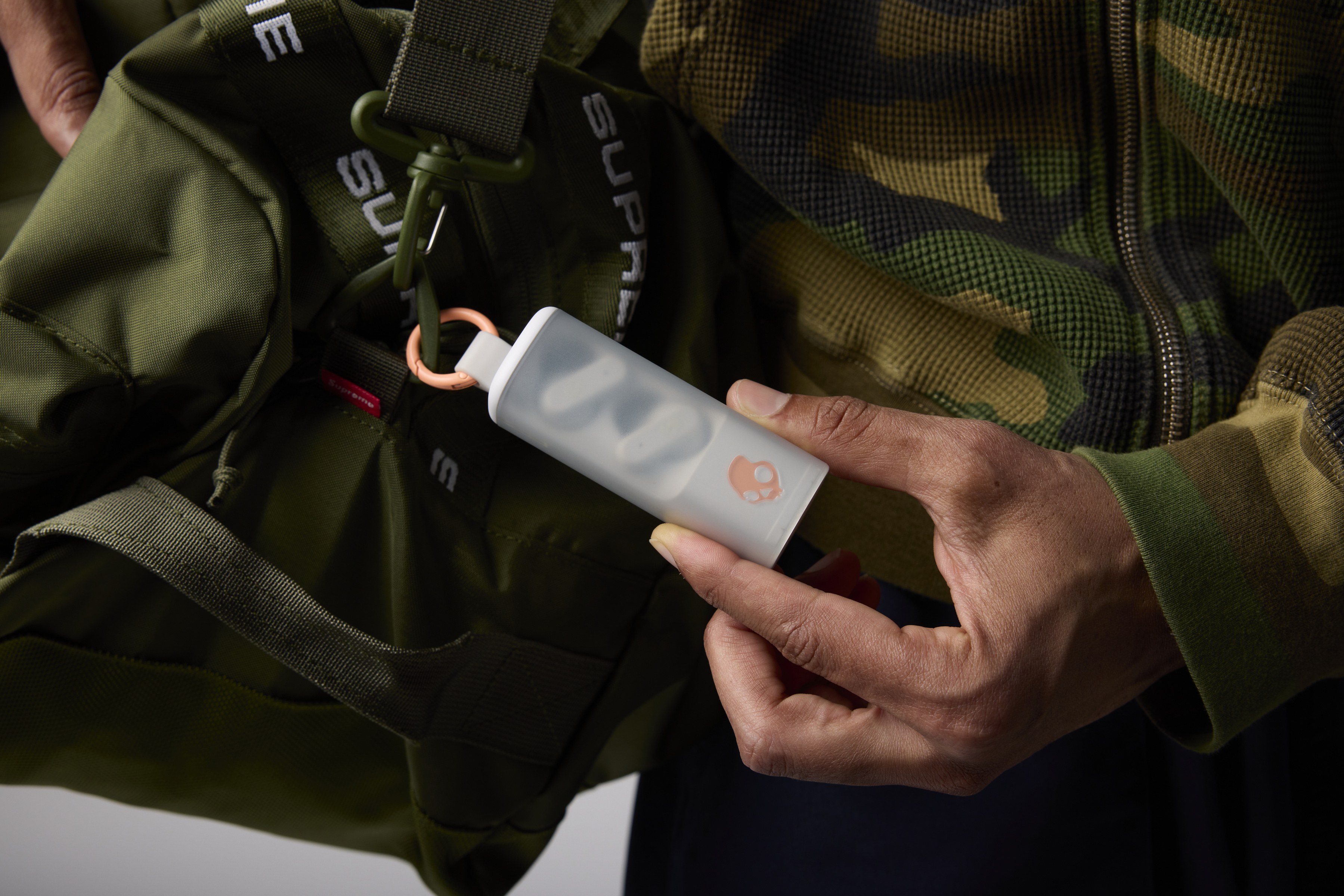 Osoba trzyma przezroczystą plastikową kapsułkę z małymi przedmiotami. Widoczna zielona torba.