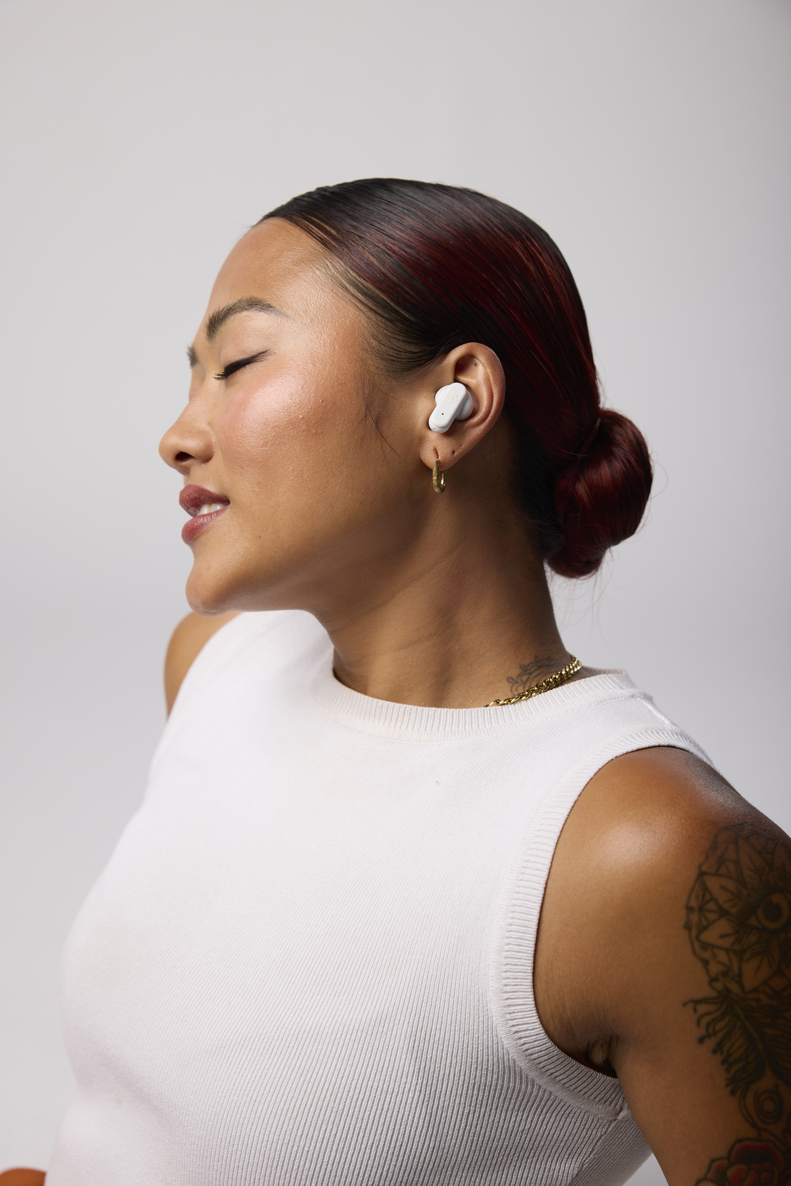 Kobieta z białymi słuchawkami, w białym topie i koku. Słuchawka w uchu. Białe tło.