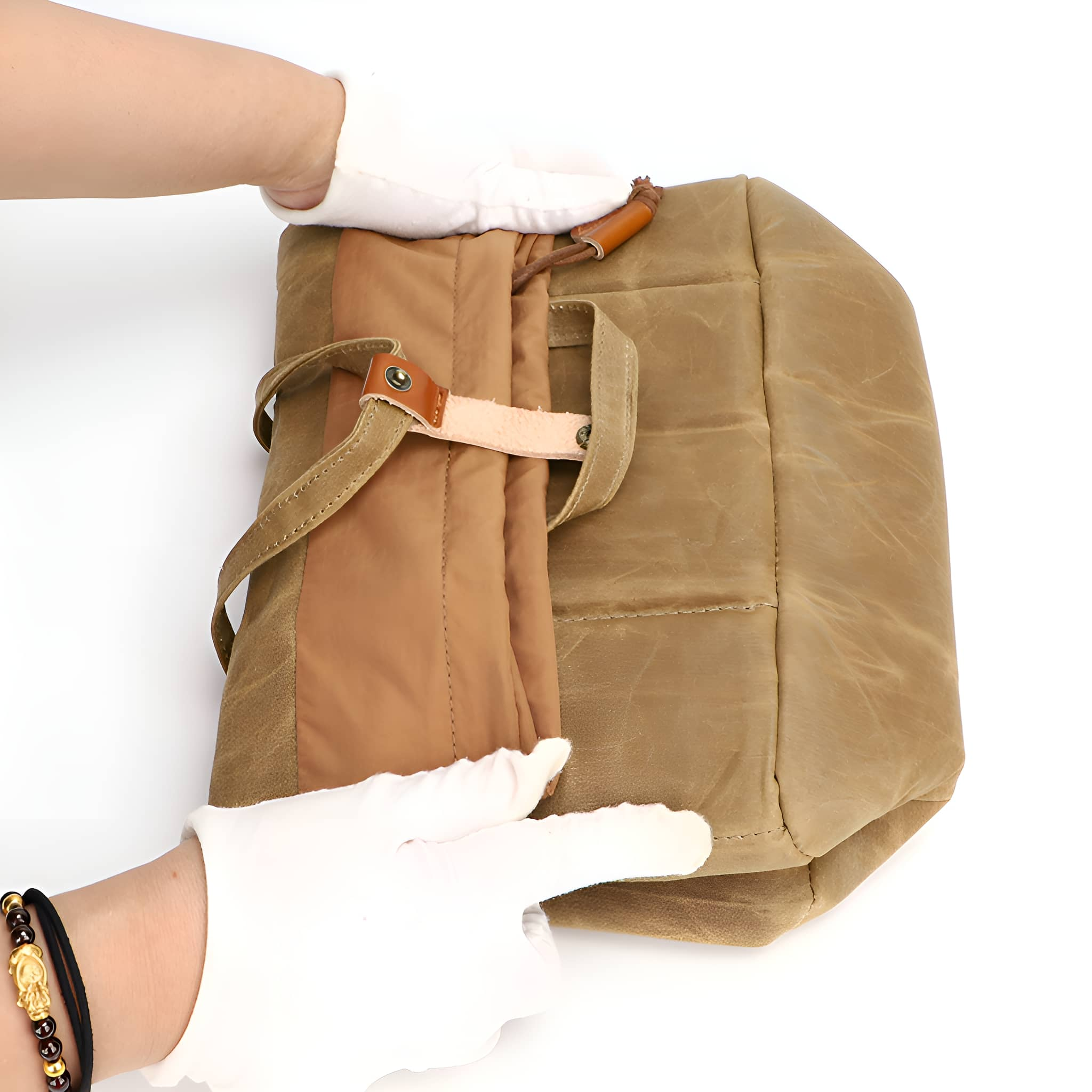 Hände mit weißen Handschuhen, die eine Segeltuchtasche mit braunem Lederriemen falten.