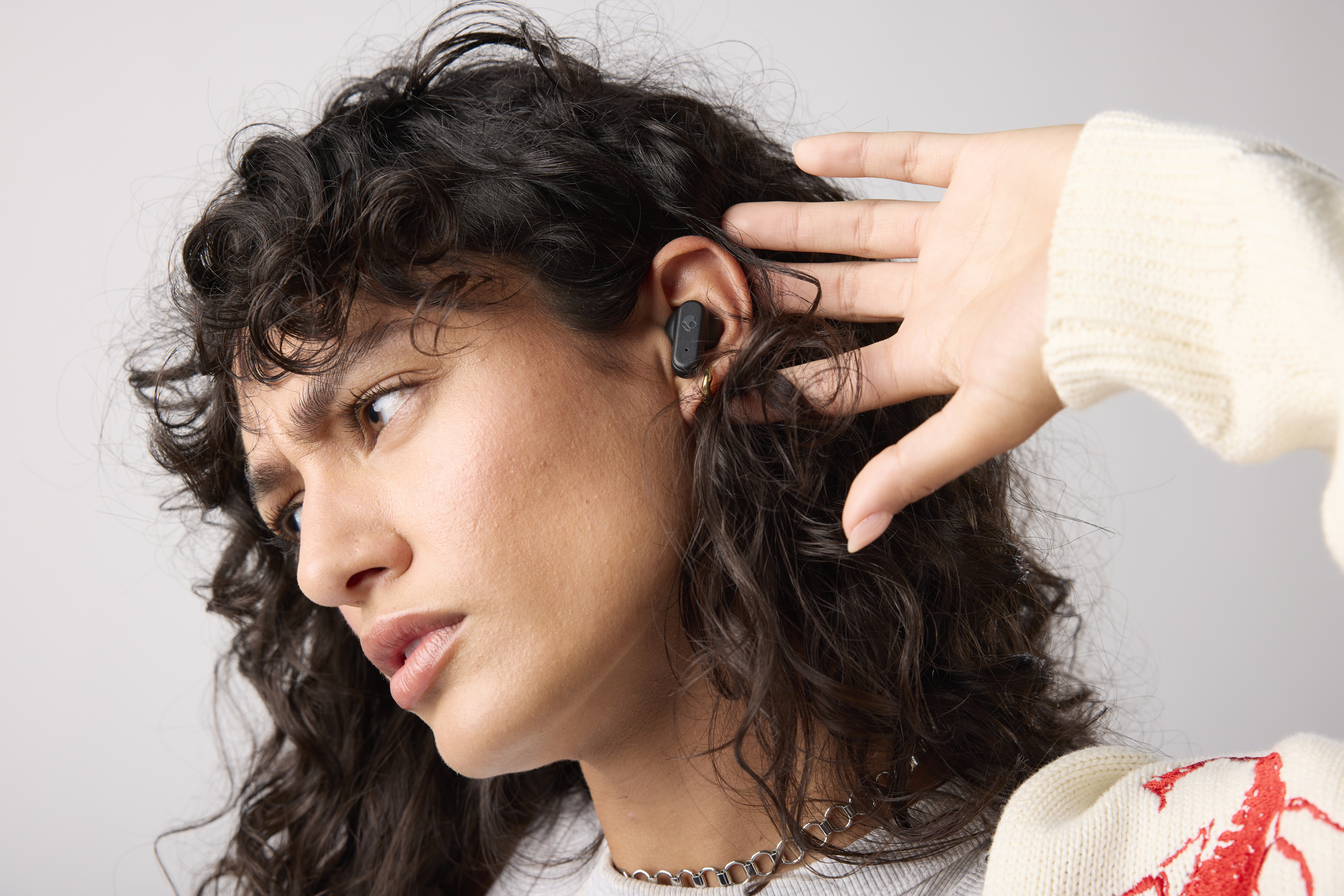 Kobieta z kręconymi włosami w słuchawkach. Dotyka ucha. Słuchawki są czarne.